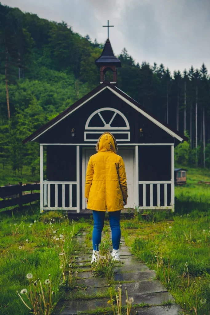 Woman in yellow hooded jacket standing facing a backyard shed
